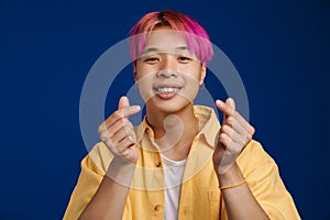 Asian boy with pink hair smiling while rubbing his fingers