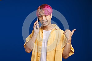 Asian boy pointing finger aside while talking on cellphone