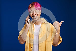 Asian boy pointing finger aside while talking on cellphone