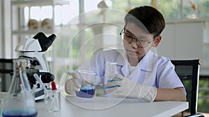 Asian boy pouring blue liquid during learn chemistry at laboratory