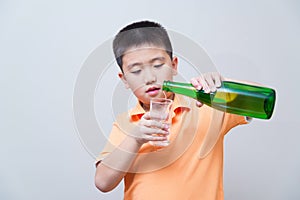 Asian boy pouring water into glass from a green bottle,