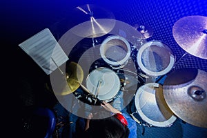 Asian boy put blue shirt and red headphone to learning and play drum set with wooden drumsticks in music room. The concept of