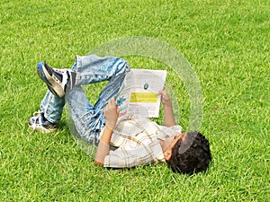 Asian boy reading on lawn