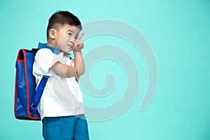 Asian boy in a school uniform with backpack pointing up on copy space isolated on green background.