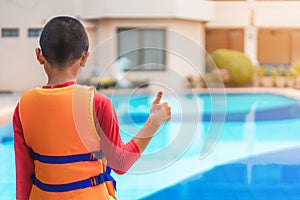 Asian boy show sign thumb up and wear life jacket near the swimming pool
