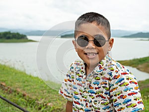 An Asian boy sitting and wearing glasses On the background of the reservoir at the tourist attractions in Thailand