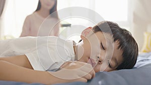 Asian boy sleeping in bed in the morning while mother sitting in background