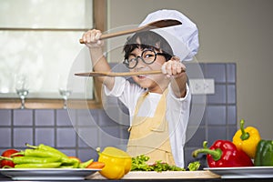 Asian Boy son cooking salad food holdind wooden spoon with vegetable holding tomatoes and carrots, bell peppers on plate for happy