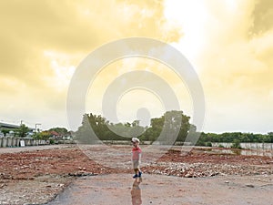 Asian boy stand alone in the demolition wasteland construction area at the sunset time with raylight and cloudy.