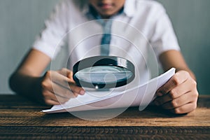 Asian boy student looking at paper using magnifying glass.