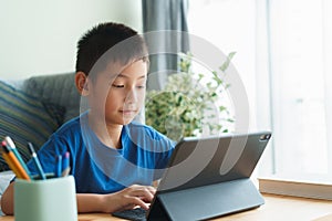 Asian boy is studying online via the internet on tablet while sitting in the living room in morning, Asia child watching and