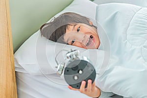 Asian boy upset waking up by alarm clock on bed at home in the morning, with stress and frustrated insomnia concept