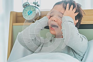 Asian boy upset waking up by alarm clock on bed at home in the morning, with stress and frustrated insomnia concept