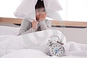 Asian Boy wake up late on seven AM and lazy to go to school. Closed up and focus on clock on white bed in bedroom