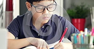 Asian boy waring eyeglass and doing your homework at home.
