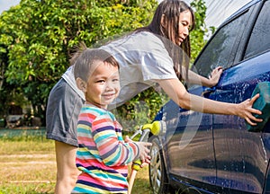 Asian boy washing blue car by green water sprayer