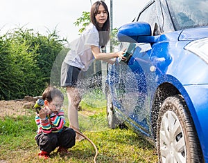 Asian boy washing blue car by green water sprayer