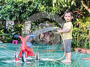 Asian boy washing red bicycle by green water sprayer