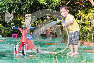 Asian boy washing red bicycle by green water sprayer