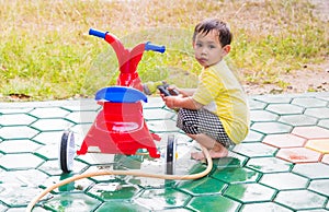 Asian boy washing red bicycle by green water sprayer