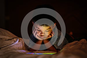 Asian boy watching colorful bright tablet screen in dark.