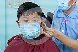 An Asian boy wearing a mask cut his hair in a barber shop. To prepare for school During the coronavirus outbreak. New normal