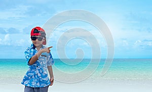 Asian boy wearing sunglasses and a summer outfit is pointing at a free space on the background