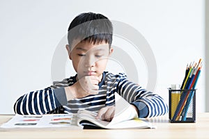 Asian boy who are studying in elementary school reading and doing homework by himself at home