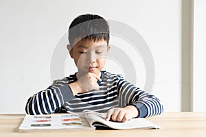 Asian boy who are studying in elementary school reading and doing homework by himself at home