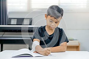 An asian boys at the wounded hands weary of writing a notebook.