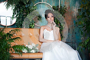 Asian bride with flowers in white dress sitting on sofa