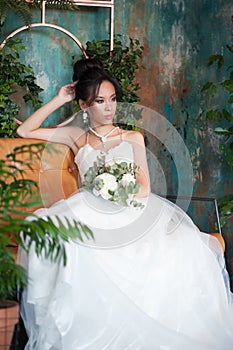 Asian bride with flowers in white dress sitting on sofa