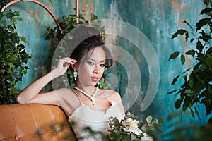 Asian bride with flowers in white dress sitting on sofa