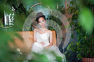 Asian bride with flowers in white dress sitting on sofa