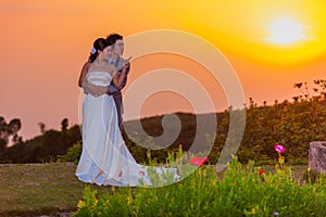 Asian Bride and Groom Standing on Mountain at Sunset