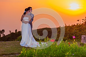 Asian Bride and Groom Standing on Mountain at Sunset