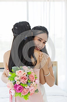 An Asian bride in a white wedding dress embraces her friend in a pink dress with a smile, then shows a diamond ring on her left