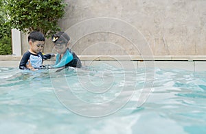 Asian brother help and support his little brother to play and swimming in the pool