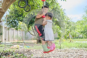 Asian brother and sister having fun playing with outdoor tree hanging rope swing toy at backyard