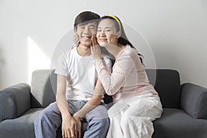 Asian brother and sister hugging with care and love sit on sofa.