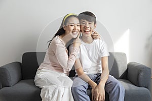 Asian brother and sister hugging with care and love sit on sofa.