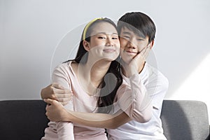 Asian brother and sister hugging with care and love sit on sofa.