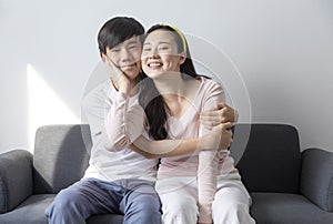 Asian brother and sister hugging with care and love sit on sofa.