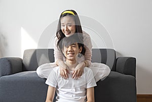 Asian brother and sister hugging with care and love sit on sofa.