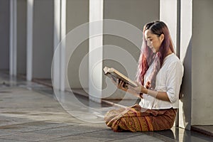 Asian buddhist woman is reading Sanskrit ancient Tripitaka book of Lord Buddha dhamma teaching while sitting in temple to chant