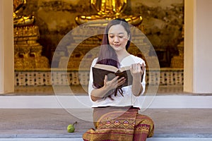 Asian buddhist woman is reading Sanskrit ancient Tripitaka book of Lord Buddha dhamma teaching while sitting in temple to chant