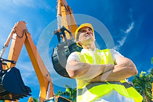 Asian builder in front of shovel excavator