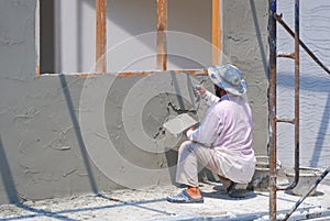 Asian builder is plastering cement wall inside of room in house construction site