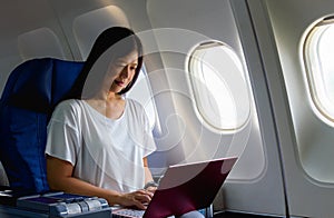 Asian businees woman passenger using laptop on board for working while sitting in airplane. Traveling and technology image concept