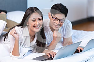 Asian business couple team working at home on the bed with laptop happy enjoy with success portrait looking camera